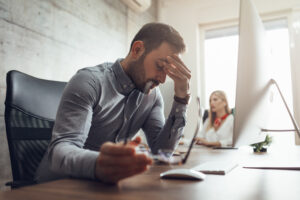 Young handsome frustrated and stressed businessman sitting at the office front a computer and holding head.