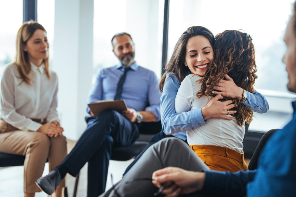 The two women are attending a group therapy session. They are showing support and kindness. Portrait of female psychologist embracing young woman during therapy session in support group